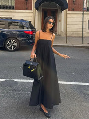 Woman in a black dress holding a black handbag on a city street.