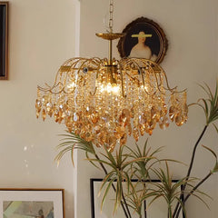 Gold chandelier with crystal accents in a room with plants and framed pictures.