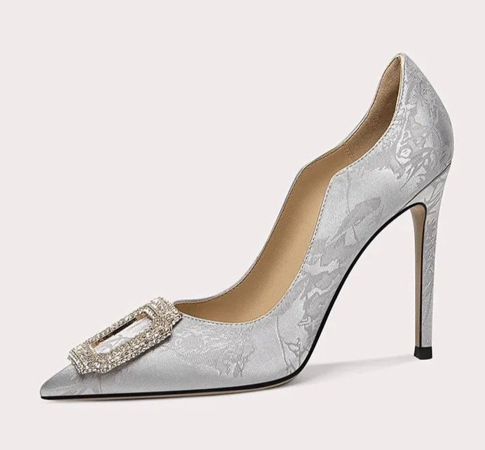 Silver high-heeled shoe with decorative buckle on a white background