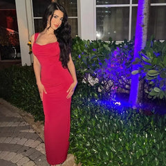 Woman in a red dress standing outdoors at night with greenery and blue lights in the background.