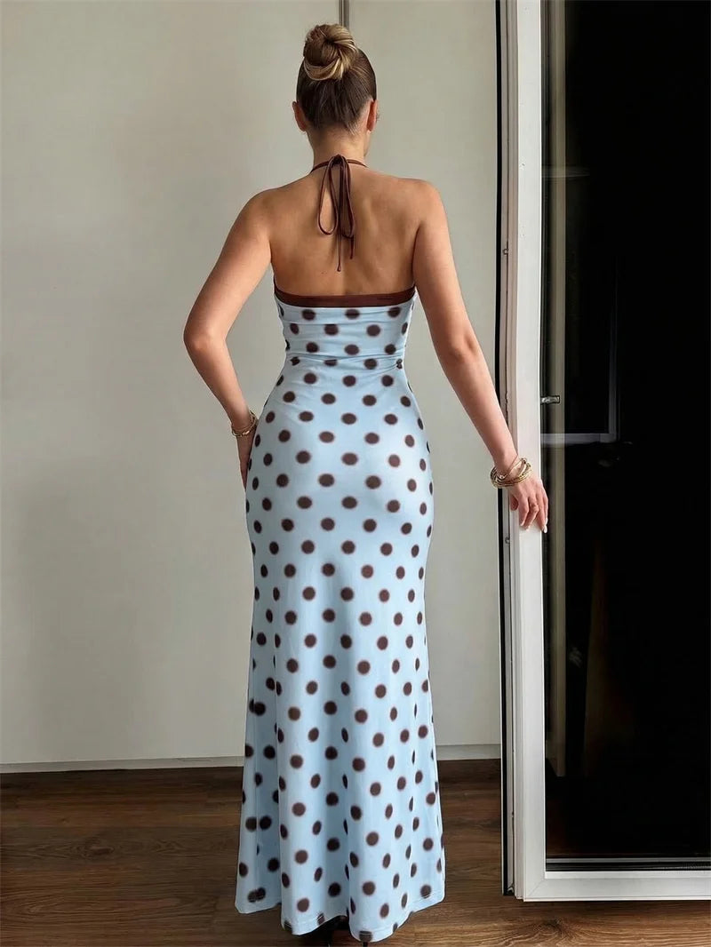 Woman wearing a polka dot dress standing in a room with a neutral wall and wooden floor.