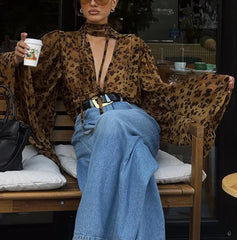 Person wearing a leopard print top and blue jeans sitting on a wooden bench.