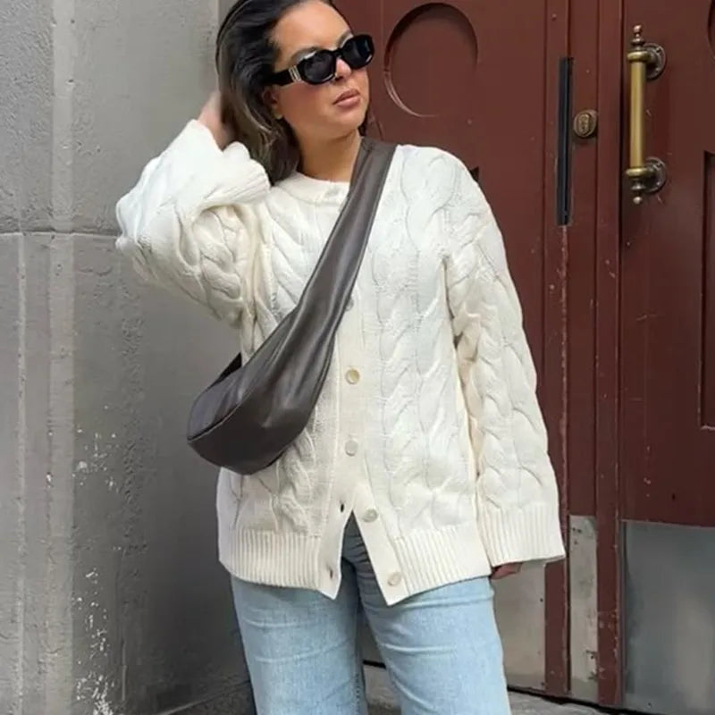 Woman wearing a white cable knit sweater and sunglasses, standing against a red door.