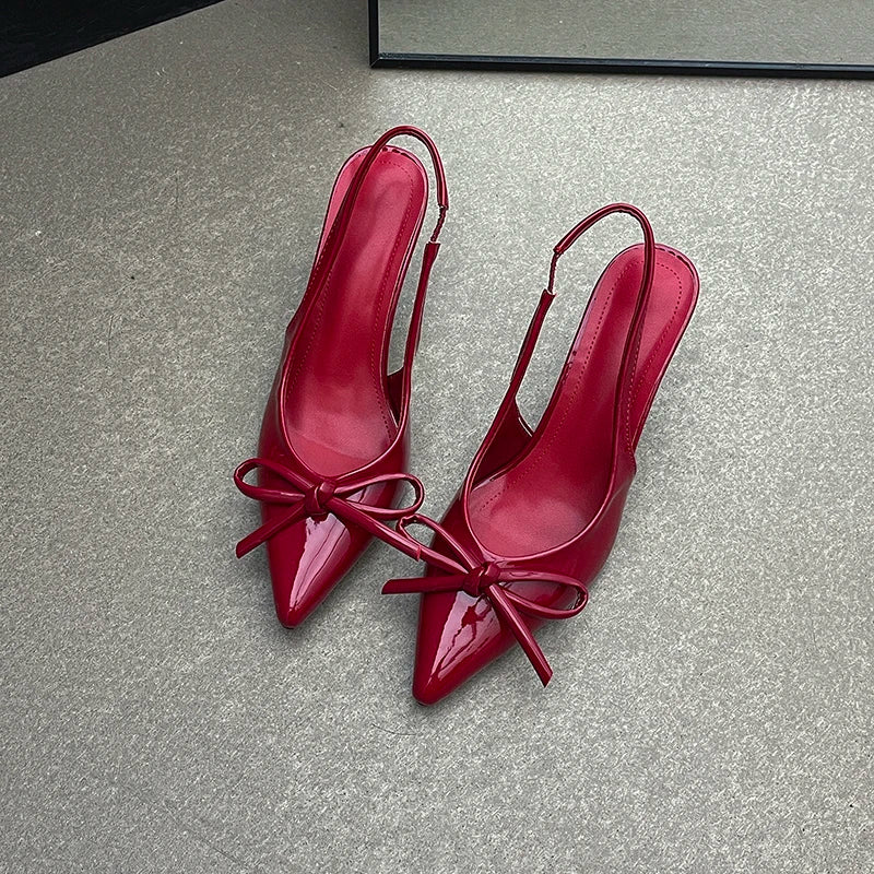 Pair of red high-heeled shoes with bow details on a gray surface