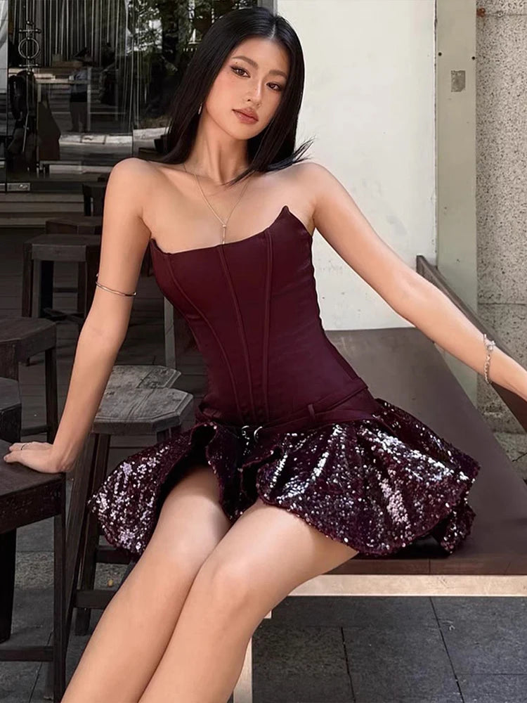 Woman in a burgundy dress with sequin skirt sitting on a bench outdoors.