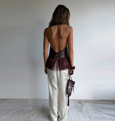 Woman wearing a backless dress with sheer panels and white pants, standing against a plain wall.