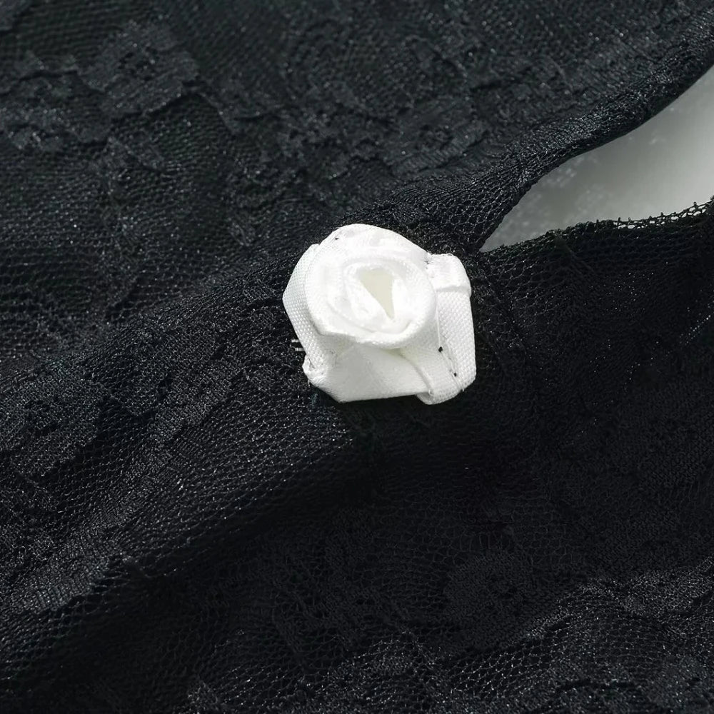 Close-up of a black lace fabric with a white rose flower brooch.