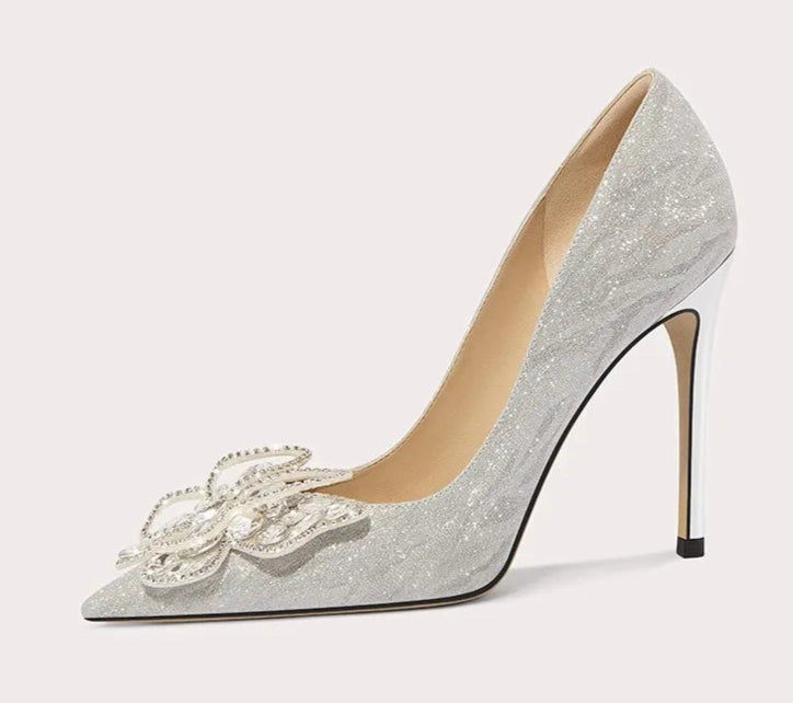 Silver high-heeled shoe with decorative bow on a light gray background