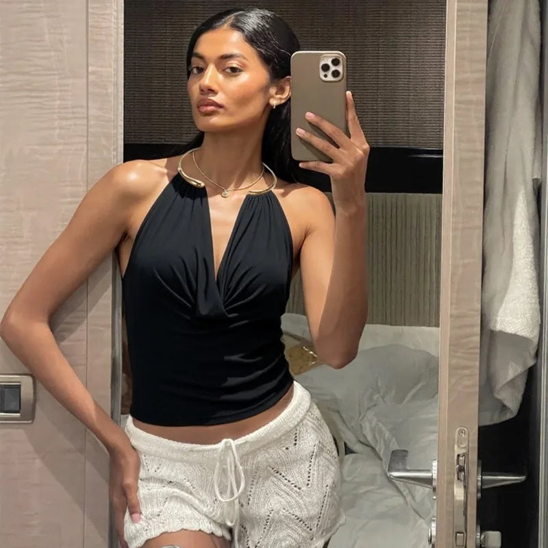 Woman taking a mirror selfie wearing a black top and white shorts in a bedroom setting.