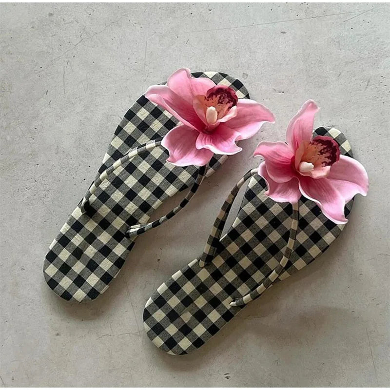 Black and white checkered flip-flops with pink floral decorations on a gray surface
