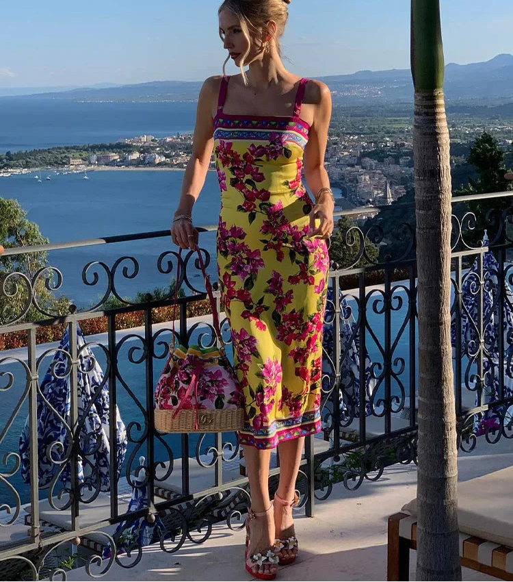 Woman in a colorful dress standing on a balcony with a scenic view of the sea and mountains.