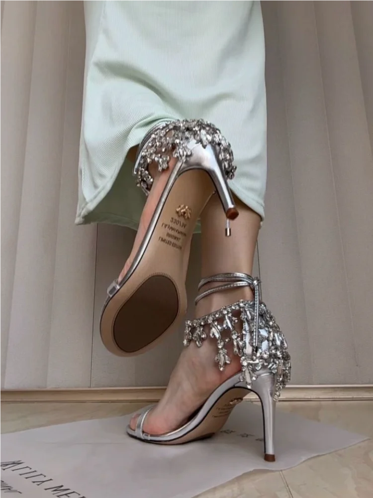 Silver high-heeled shoes with embellishments on a neutral background