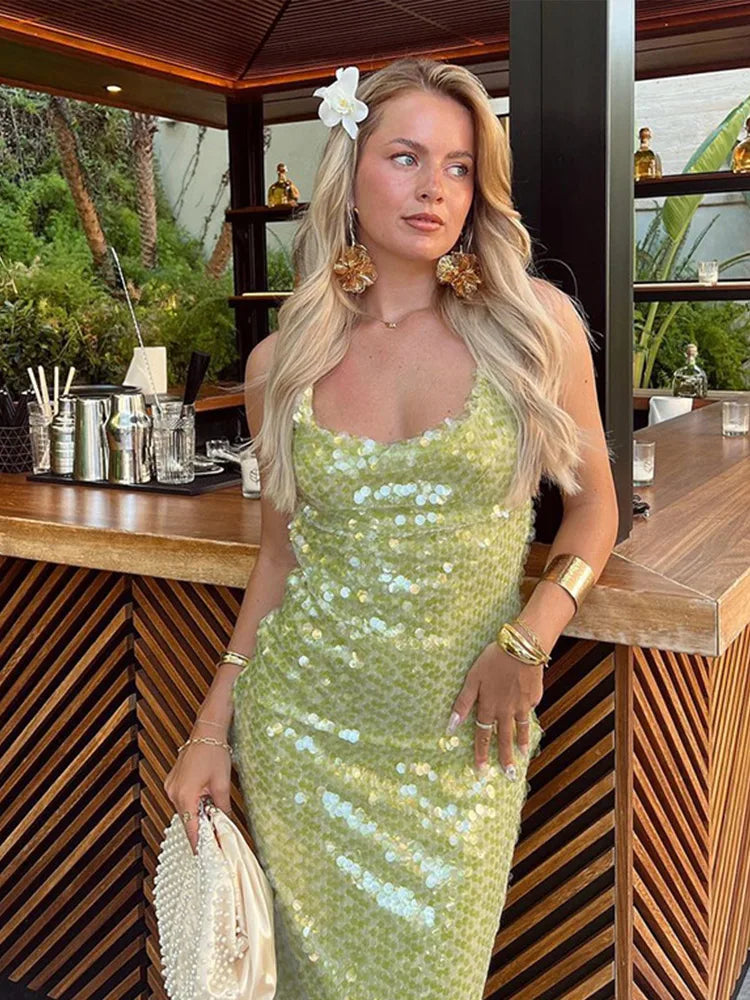 Woman in a green sequin dress standing in a tropical outdoor setting.