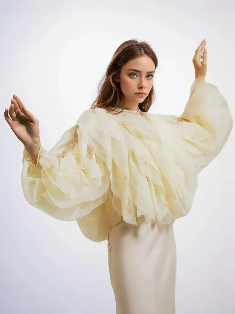 Woman wearing a cream-colored outfit with large sleeves against a white background