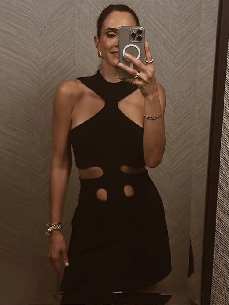 Person wearing a black dress with cut-out design in front of a textured wall.