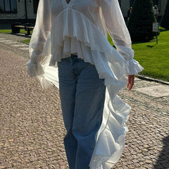Person wearing a white ruffled blouse and blue jeans on a paved path.