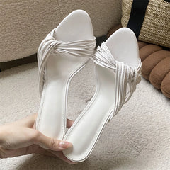 White twisted strap stiletto heels held by hand