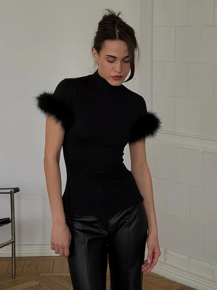 Woman wearing a black turtleneck with fluffy shoulders in a room with white tiled walls.