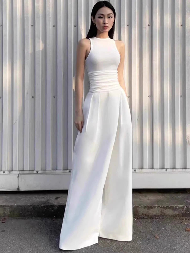 Woman wearing a white sleeveless dress standing against a corrugated metal wall.