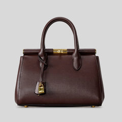 Dark brown structured top-handle satchel bag with gold clasp and lock detail against a grey background.