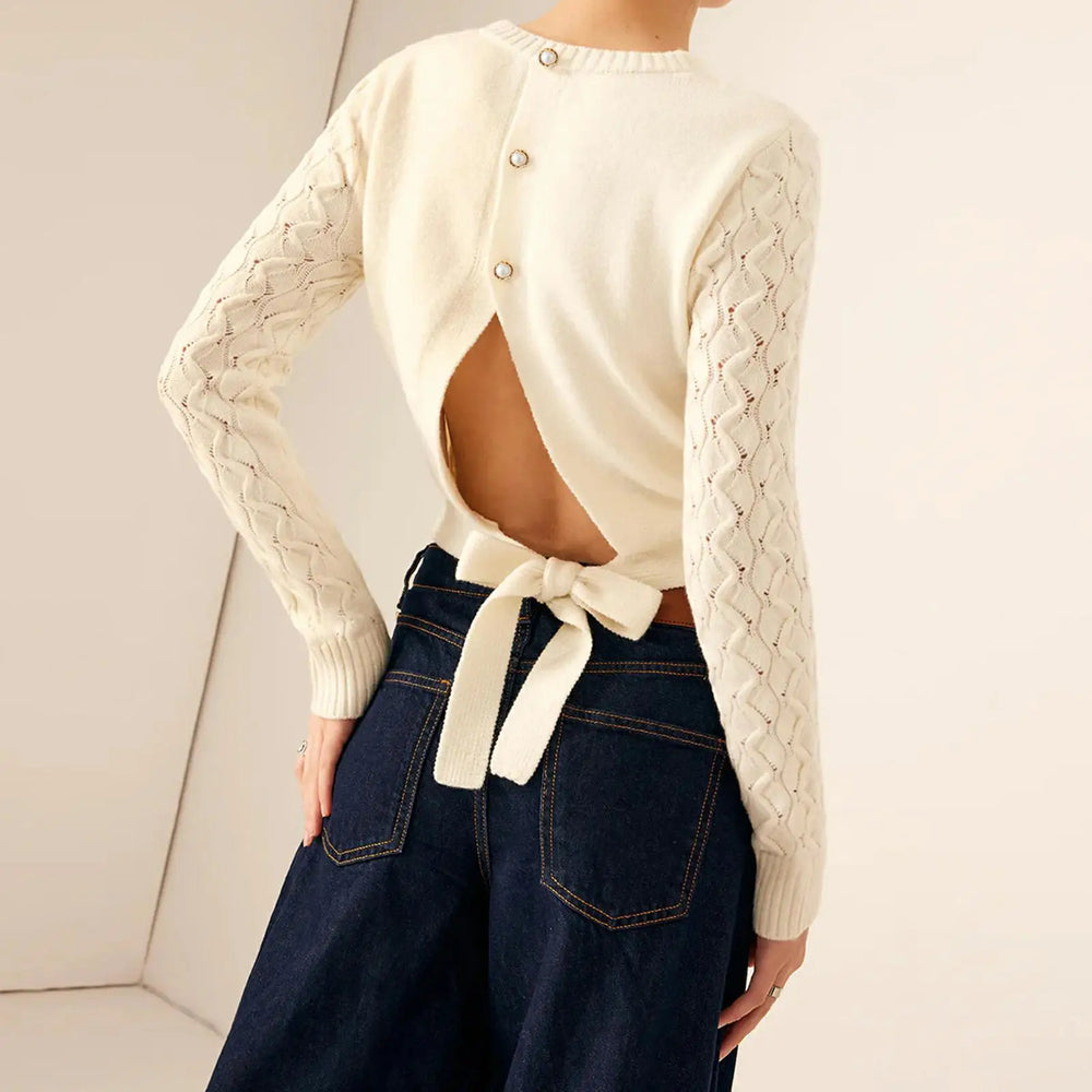 Person wearing a cream cardigan with braided sleeves and tied front, paired with dark blue jeans.