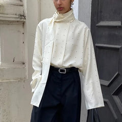 Model wearing a white polka dot blouse with a high neck and scarf detail