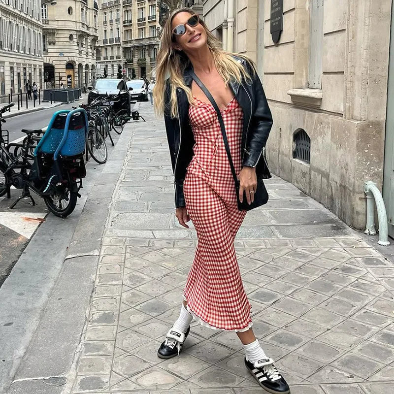 Woman in a red checkered dress and black leather jacket walking down a city street.