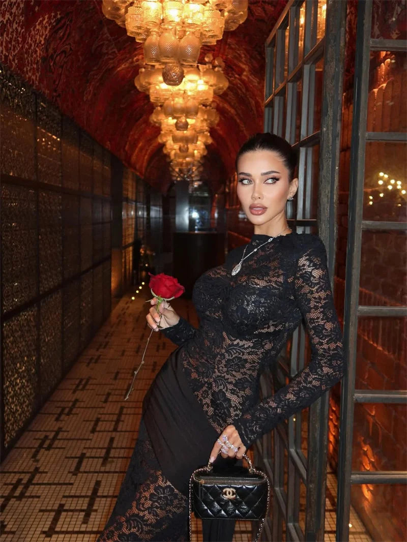 Woman in a black lace dress holding a red rose in an elegant hallway.