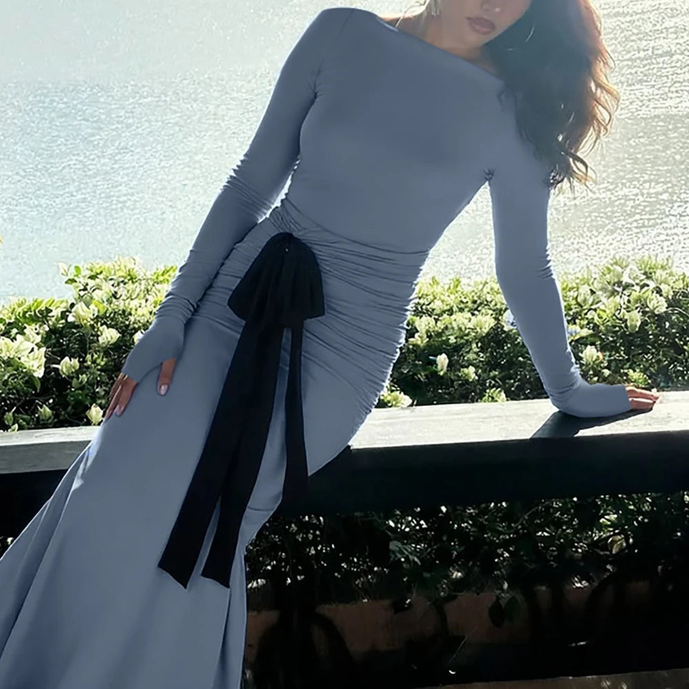 Woman wearing a long, light gray dress with a black ribbon in an outdoor setting.