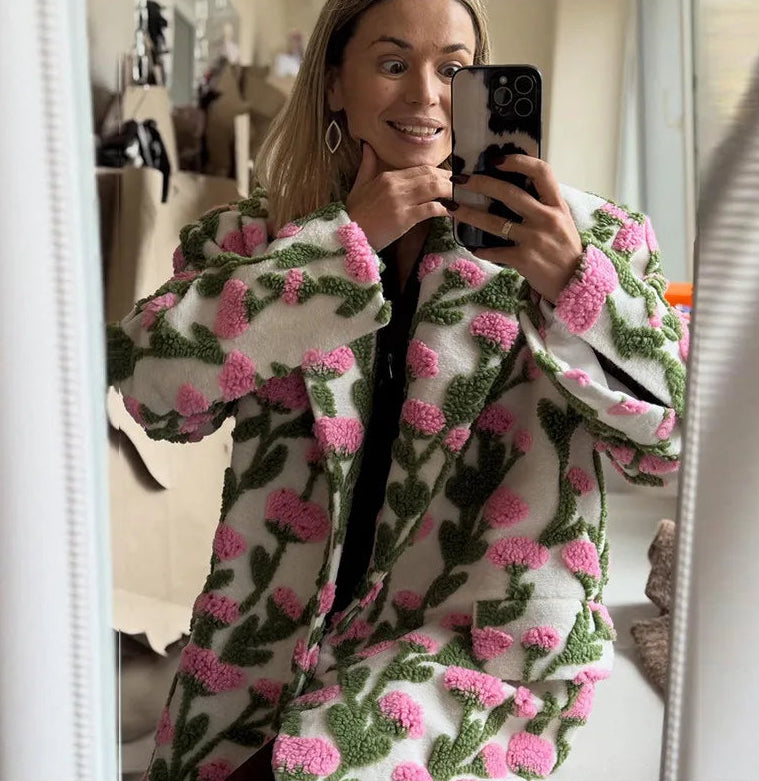 Woman taking a mirror selfie wearing a floral patterned coat.