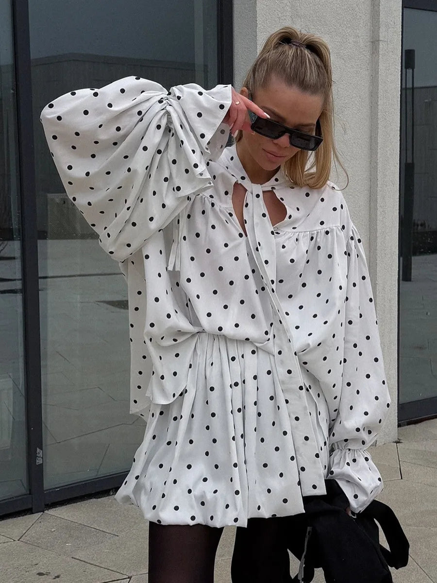 Woman wearing a white polka dot blouse with puffed sleeves outdoors.