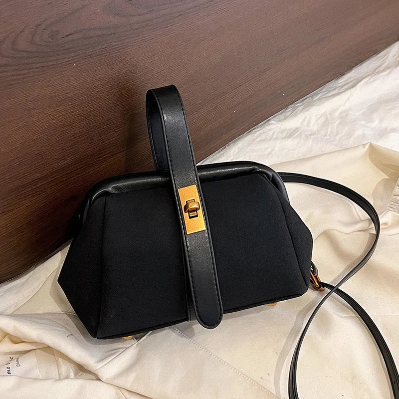 Black handbag with a gold clasp on a white fabric background