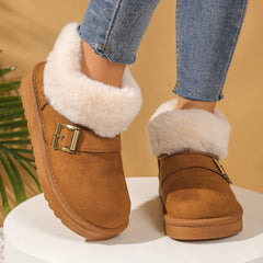 Brown suede boots with white fur trim and gold buckles worn with blue jeans on a beige background.