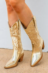Gold cowboy boots worn by a person on a neutral background