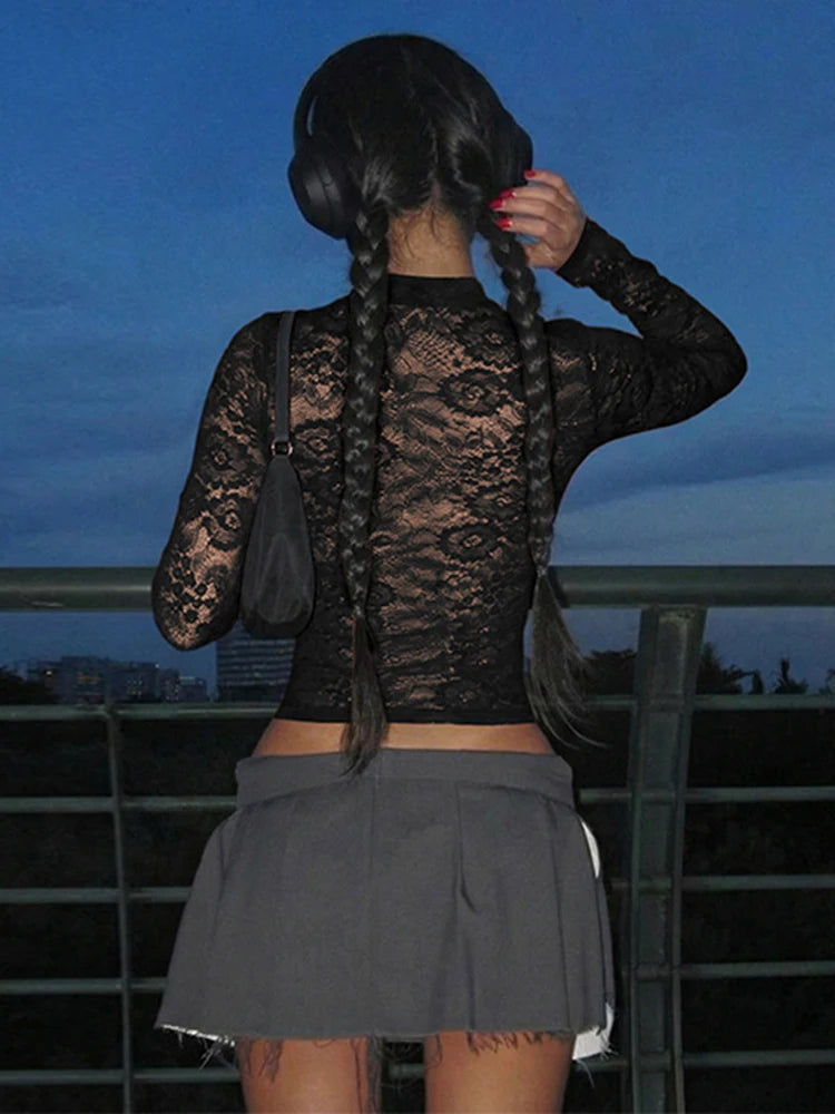 Person wearing a black lace top and gray skirt with braided hair, standing against a dark sky.