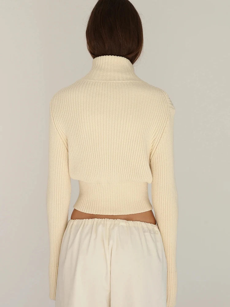 Person wearing a beige ribbed sweater and pants against a plain background
