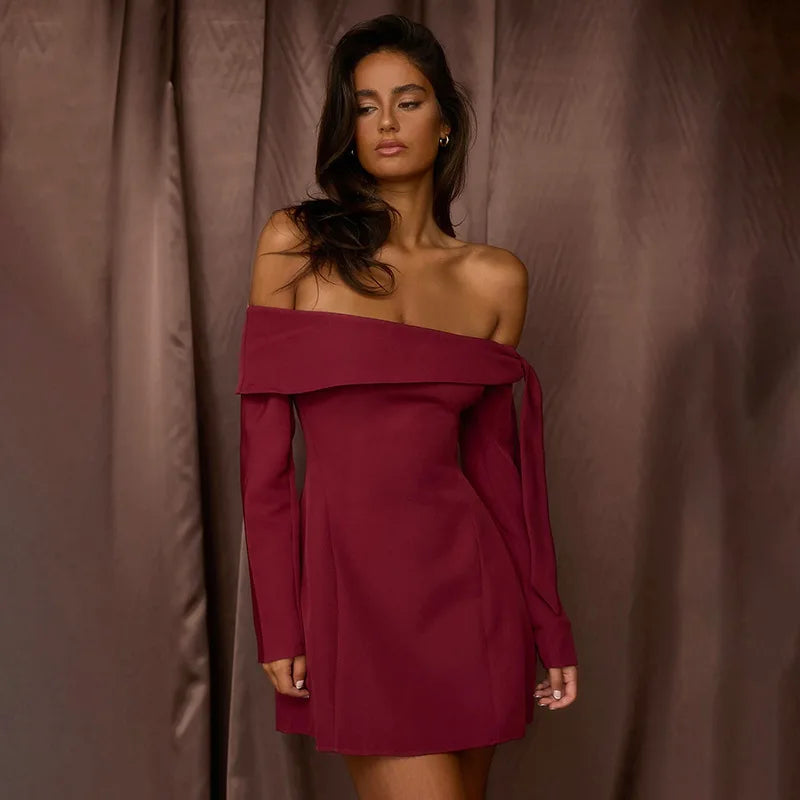 Woman wearing a burgundy off-shoulder dress against a brown curtain background
