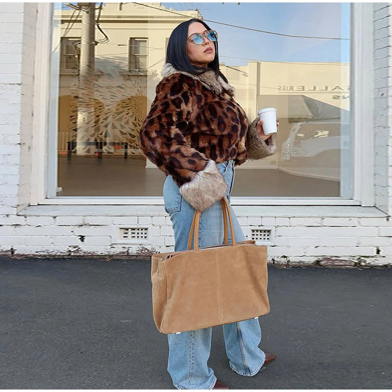 Person wearing a leopard print jacket and holding a brown bag, standing in front of a store window.