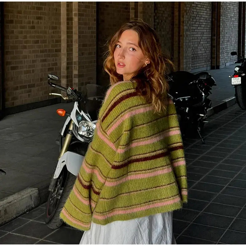 Woman wearing a green striped sweater standing on a sidewalk with motorcycles in the background