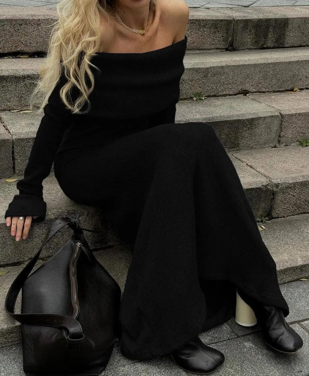 Person wearing a black off-shoulder dress sitting on steps with a black handbag beside them.