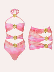 Pink and white tie-dye one-piece swimsuit with cutouts and gold flower accents, paired with a matching skirt.