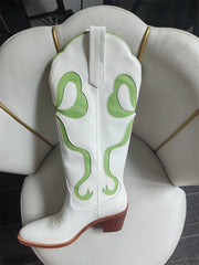 White cowboy boot with green snake patterns on a white chair.