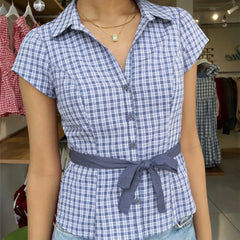 Person wearing a blue and white checkered shirt with a belt in a clothing store.