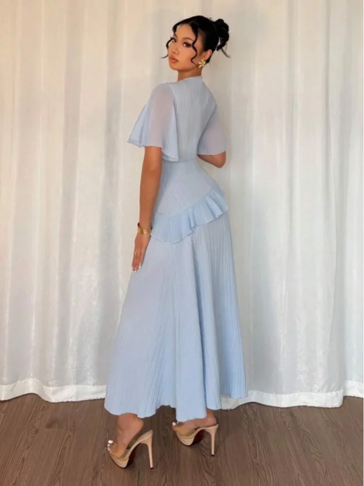 Woman wearing a light blue dress standing against a white curtain.
