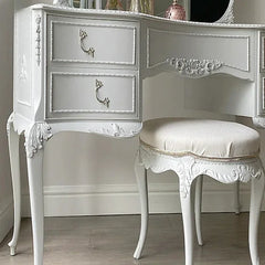 White ornate vanity desk with matching stool against a neutral wall.