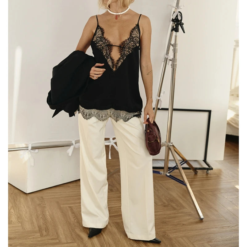 Person wearing a black lace top and white pants in an indoor setting.