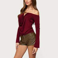 Woman wearing a burgundy off-shoulder top and brown leather shorts on a light gray background