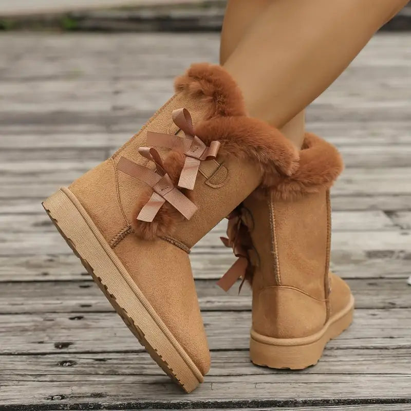 Tan suede boots with fur trim and ribbons on a wooden floor.