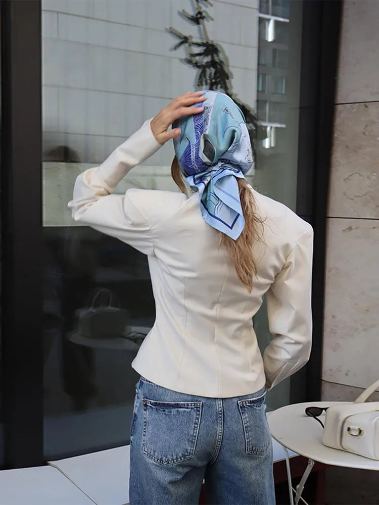 Person wearing a white shirt and blue jeans, adjusting a patterned scarf on their head.