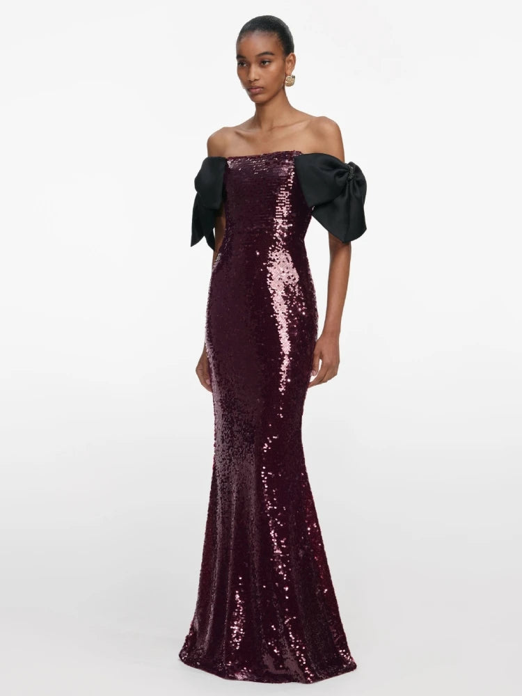 Woman wearing a dark purple sequin off-shoulder gown on a white background